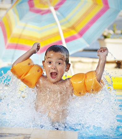 Malý chlapec s nadšeným výrazem skáče do vody v bazénu